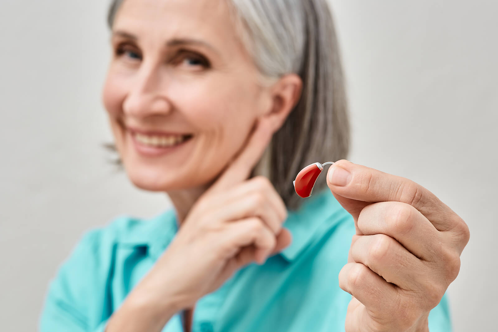 Woman holding hearing aid and pointing at ear